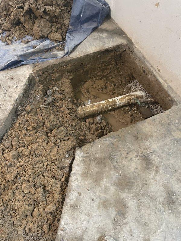 Performed concrete floor excavation in basement to provide access for new sewer line installation. Created rectangular opening in concrete foundation, exposing existing underground piping system that required replacement. Removed soil and debris to establish proper depth and clearance for new sewer line routing into the residence, with work area prepared for subsequent pipe installation and connection to main system.