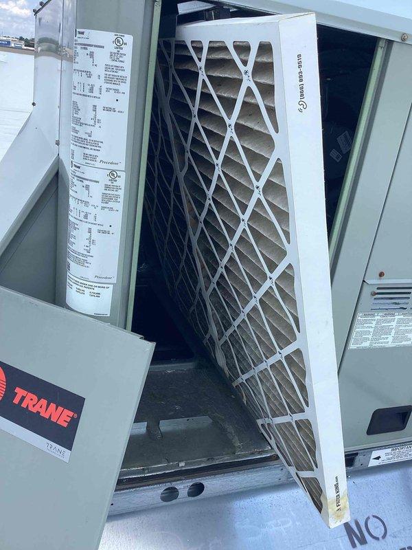 Responded to no cooling complaint in front area with afternoon cooling issues in back unit. Upon inspection, discovered severe heat damage and deterioration to ductwork components, with extensive charring and oxidation along panel seams and joints. Temperature reading of 87.4°F confirmed inadequate cooling performance. Inspected Trane RTU and found compromised air filter requiring replacement. Replaced allergen filter and assessed heat-damaged ductwork sections for necessary repairs to restore proper system operation and airflow distribution.