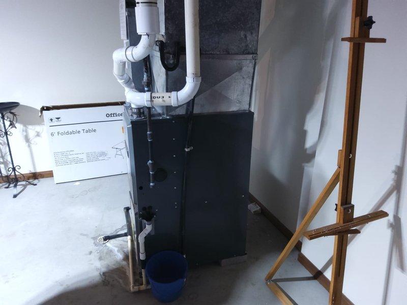 Completed comprehensive HVAC estimate for AC retrofit installation in residential basement mechanical room. Assessed existing furnace and air handling equipment, evaluated ductwork configuration including gray return air ducts and overhead galvanized steel components, and documented current PVC condensate drainage system with white piping running to floor drain. Photographed existing multi-unit HVAC setup, noting wall-mounted control panel, thermostat placement, and exposed ceiling joist structure to determine optimal retrofit approach for new air conditioning system integration with current heating infrastructure.