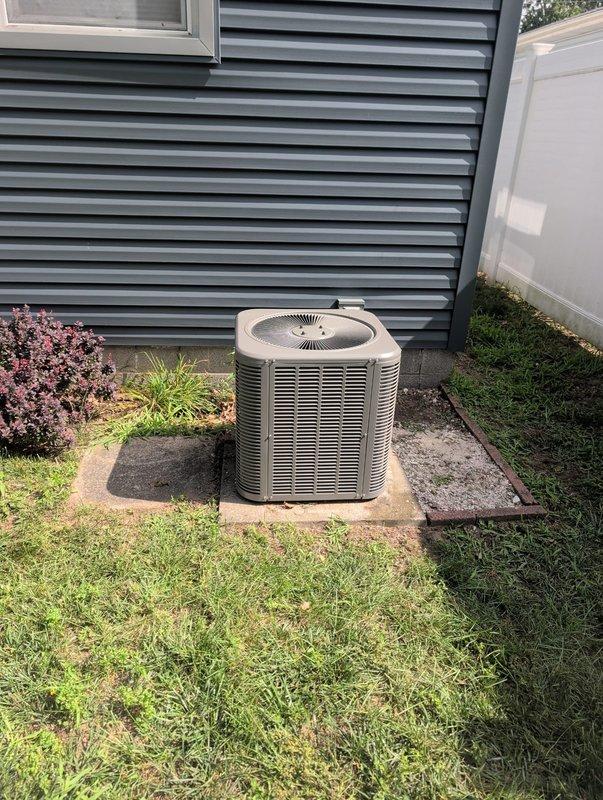 Completed full AC retrofit installation including outdoor condensing unit and indoor evaporator coil. Installed new beige cylindrical air conditioning unit on composite pad adjacent to building exterior with proper clearances maintained. Unit features horizontal ventilation slats and top-mounted fan grille for optimal airflow. Connected indoor evaporator coil to existing furnace system in basement mechanical room, integrating with current HVAC infrastructure. Verified proper refrigerant lines, electrical connections, and condensate drainage. System tested and operational, providing efficient cooling capacity for residential structure.