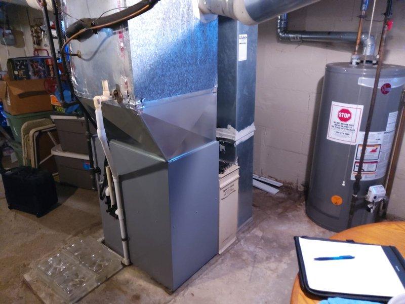 Completed comprehensive AC system retrofit including installation of new air handler unit in basement mechanical room and outdoor condenser unit. Air handler features modern blue filter section for improved air quality and ease of maintenance, integrated seamlessly with existing ductwork and utility infrastructure. Outdoor condenser unit positioned on concrete pad against exterior wall with proper clearance maintained from surrounding landscaping elements including ornamental grasses and shrubs for optimal airflow and service access.