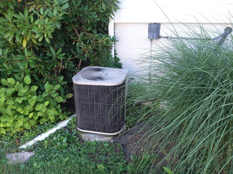 Completed comprehensive AC system retrofit including installation of new air handler unit in basement mechanical room and outdoor condenser unit. Air handler features modern blue filter section for improved air quality and ease of maintenance, integrated seamlessly with existing ductwork and utility infrastructure. Outdoor condenser unit positioned on concrete pad against exterior wall with proper clearance maintained from surrounding landscaping elements including ornamental grasses and shrubs for optimal airflow and service access.