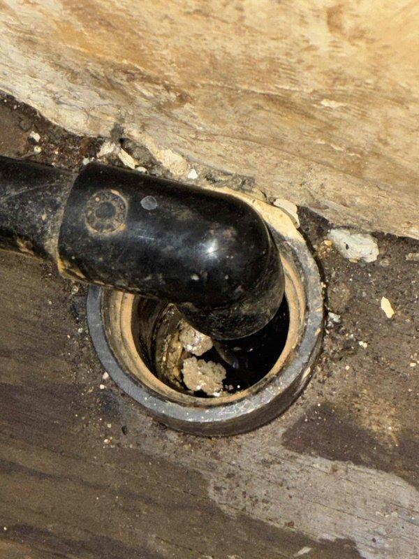 Responded to callback for water discharge issue at furnace location. Previous technician had identified potential plumbing concern, but plumber determined issue was HVAC-related. Upon arrival, inspected furnace area and located Aspen refrigerant evaporator unit installed in concrete housing showing signs of moisture accumulation and condensate drainage problems. Examined floor drain assembly with P-trap configuration in vicinity of equipment, noting debris accumulation and age-related deterioration around drain fixture. Documented existing conditions with photographs showing evaporator unit installation, concrete enclosure with visible moisture staining and efflorescence, and floor drain assembly condition. Confirmed water discharge originating from HVAC equipment condensate system rather than plumbing infrastructure.