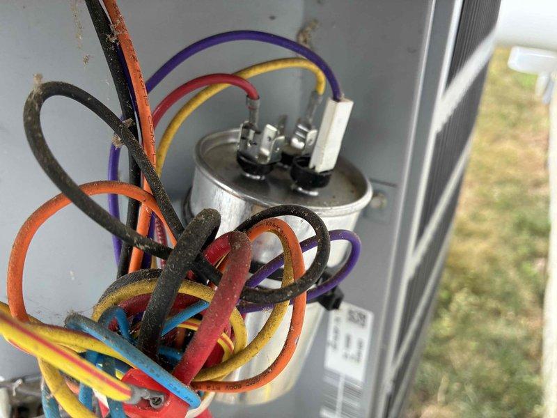 Responded to service call for air conditioning unit with reported leaking in bottom drain pan. Upon arrival, performed visual inspection of outdoor condensing unit. Examined electrical components including capacitor and associated wiring connections, noting normal wear and dirt accumulation consistent with outdoor exposure. Inspected condenser coil fins for debris buildup and blockage. Checked drain pan area for signs of water accumulation and potential condensate drainage issues. Documented unit condition with photographs showing interior electrical components and exterior housing. All wiring connections appeared secure with no signs of electrical failure or immediate safety concerns.