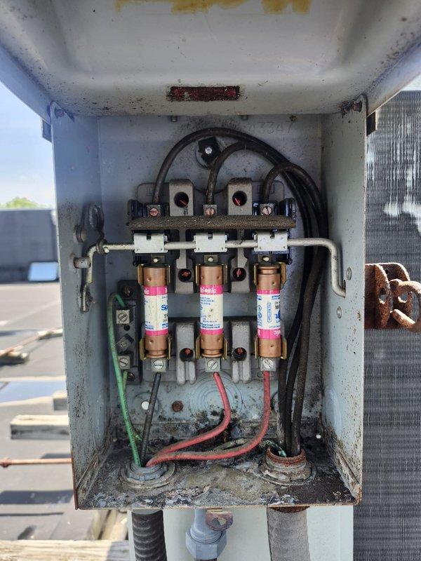 Conducted comprehensive estimate evaluation of commercial rooftop HVAC units. Assessed two RTU systems, documenting significant weathering and corrosion on exterior components, deteriorated electrical disconnect box with aged fuses and oxidized terminals, and standing water issues on roof membrane affecting equipment placement. Photographed equipment conditions including condenser coils, refrigerant lines, and electrical connections to support full system replacement recommendations.
