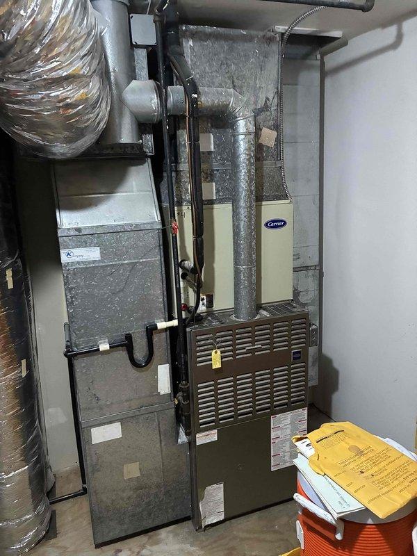 Responded to commercial A/C leak complaint and performed system inspection. Upon arrival, identified active refrigerant leak at evaporator coil connection point in air handler unit. Inspected multi-unit HVAC installation including stacked air handlers and ductwork assembly. Documented leak location with photographic evidence showing affected metallic cylindrical connection and surrounding insulation material. Verified leak source at concentric ring nozzle connection on evaporator coil inlet. Assessed overall system configuration including Carrier brand equipment, vertical ductwork routing, and associated piping. Recommended immediate refrigerant leak repair at coil connection point to restore system integrity and prevent further refrigerant loss.