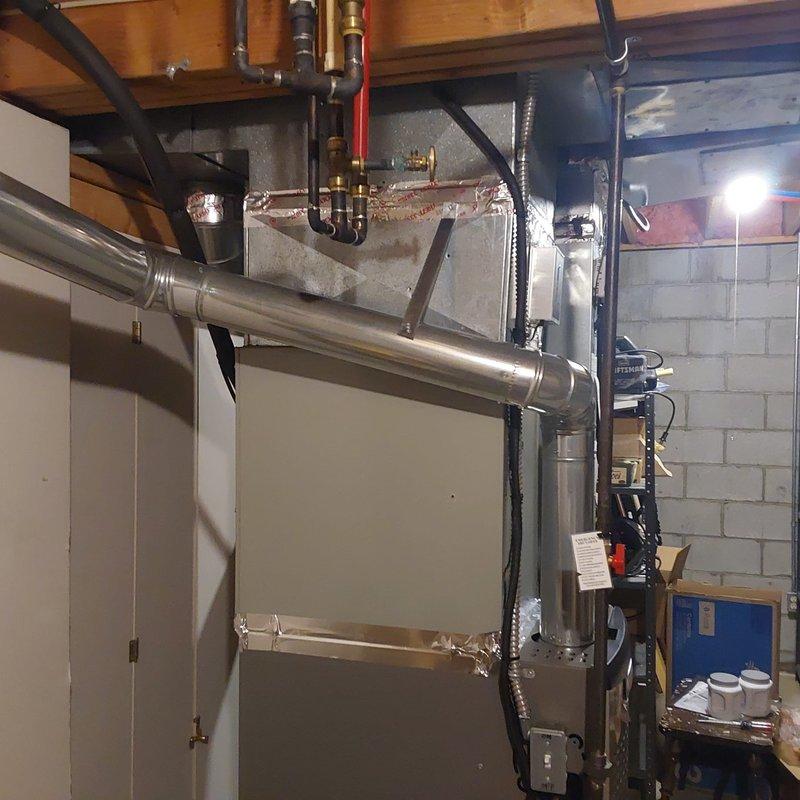 Completed AC retrofit installation in basement mechanical room. Installed new air handler unit with associated ductwork modifications, including metallic supply duct with proper sealing and insulation. Routed stainless steel exhaust flue pipe from new equipment with secure connections and proper pitch for condensate drainage. Integrated system with existing copper plumbing lines and mounted digital control panel on unit for system operation and monitoring.