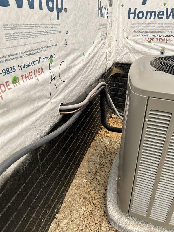 # HVAC New Construction Install

Completed installation of dual Lennox outdoor condenser units on new construction residential property. Positioned two condenser units side by side on gravel base with proper composite equipment pads for stability and drainage. Units include one black condenser and one beige/tan Lennox-branded unit, both mounted against exterior wall with Tyvek house wrap. Installed insulated refrigerant line sets with proper bending radius from top of each unit. Mounted electrical disconnect box to wall for code compliance and service accessibility. Equipment properly leveled on crushed stone base to ensure optimal performance and drainage. All refrigerant lines routed and secured according to manufacturer specifications.