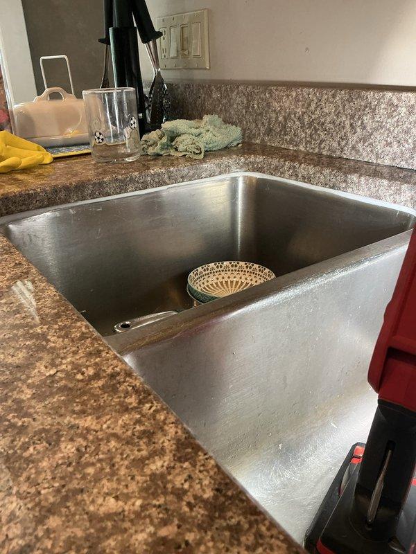 Responded to callback regarding failed silicone sealant around undermount kitchen sink. Upon inspection, discovered all previously applied silicone had deteriorated or separated from the granite countertop and sink junction. Documented existing conditions showing undermount stainless steel basin with granite countertop and backsplash. Assessed adhesion failure and prepared area for re-application of appropriate silicone sealant to restore proper water barrier and prevent moisture intrusion beneath countertop.