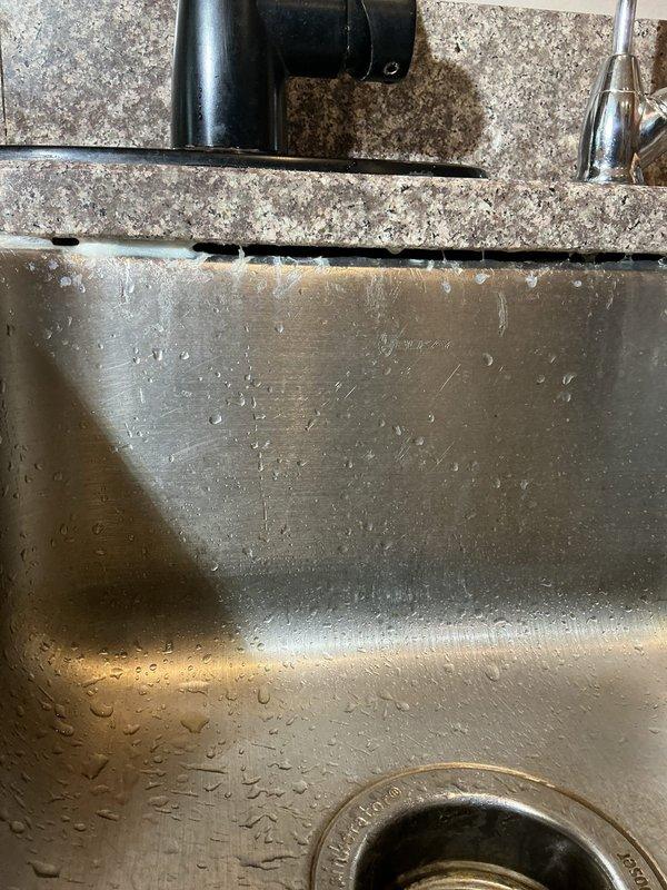 Responded to callback regarding failed silicone sealant around undermount kitchen sink. Upon inspection, discovered all previously applied silicone had deteriorated or separated from the granite countertop and sink junction. Documented existing conditions showing undermount stainless steel basin with granite countertop and backsplash. Assessed adhesion failure and prepared area for re-application of appropriate silicone sealant to restore proper water barrier and prevent moisture intrusion beneath countertop.
