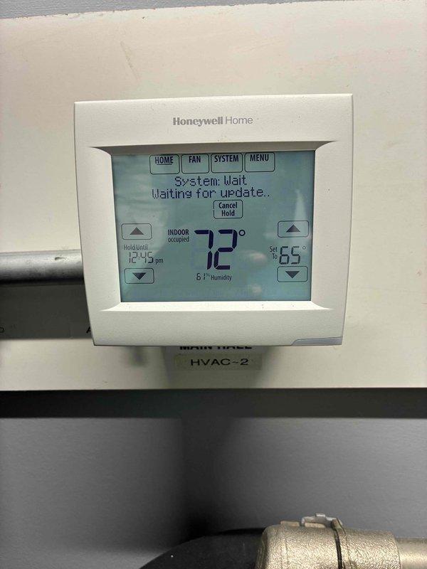 Responded to no cooling call for commercial HVAC system serving main hall area. Upon arrival, found Honeywell Home thermostat displaying "System: Wait - Waiting for update" error message with unit set to 65°F but showing actual temperature of 72°F with 61% humidity. Investigated system controls and internal components, inspecting wiring connections and electrical circuits within the air handler unit. Verified proper wire terminations and connections for yellow, black, brown, and red control wires secured with cable ties. Cleared system error, reset thermostat communication protocol, and restored normal cooling operation. System tested and verified functioning properly with thermostat responding to temperature setpoint adjustments.