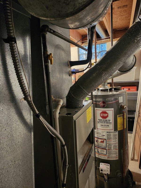 # HVAC Install - Complete System

Completed full furnace and air conditioning system retrofit in residential basement utility area. Installed new gray metal furnace/air handler unit with associated metal ductwork and flexible corrugated connections. Routed black conduit and piping from furnace to accommodate new system requirements. Connected metallic flexible ductwork with proper insulation wrapping to ceiling-mounted distribution system. Integrated new HVAC equipment alongside existing cylindrical water heater, ensuring proper clearances and access for future maintenance. Installed copper piping with expansion loop configuration and black supply lines to support system operation. All mechanical connections secured to exposed wooden framing per code requirements. System tested and verified operational upon completion.