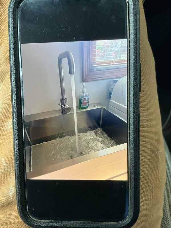 Responded to a callback for a recently installed kitchen faucet that was experiencing a leak. Upon inspection, verified the leak issue and assessed the installation including the pull-down faucet with dark finish and underlying plumbing connections. Documented the faucet assembly, stainless steel sink installation, and under-sink plumbing configuration including P-trap drainage system and braided supply lines for service records and follow-up repair work.