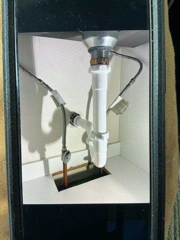 Responded to a callback for a recently installed kitchen faucet that was experiencing a leak. Upon inspection, verified the leak issue and assessed the installation including the pull-down faucet with dark finish and underlying plumbing connections. Documented the faucet assembly, stainless steel sink installation, and under-sink plumbing configuration including P-trap drainage system and braided supply lines for service records and follow-up repair work.