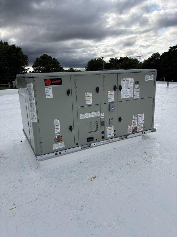 # HVAC New Construction Install Summary

Completed installation of commercial rooftop Trane HVAC unit on flat membrane roofing system with proper curb mounting. Unit secured and positioned according to manufacturer specifications with all access panels, safety labels, and operational decals properly affixed. Inside facility, installed large-scale rectangular metal ductwork system running through exposed ceiling structure with steel beam and truss support framework. Ductwork features galvanized metal construction with proper sealing and integration into building's structural grid. System configured to provide climate control for warehouse or industrial space with high ceilings and large bay door openings. All components installed per code requirements and manufacturer guidelines. Unit tested and verified operational. Installation complete and ready for commissioning.