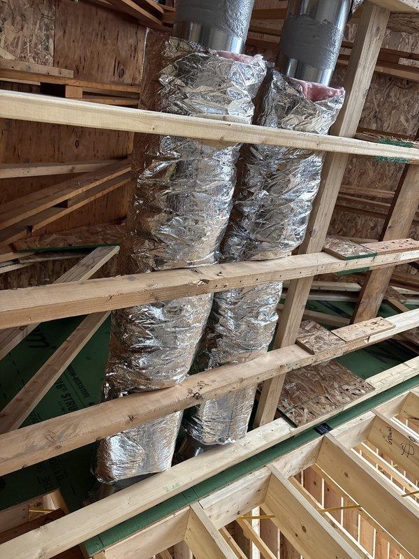 Completed rough-in and duct installation for new construction HVAC system. Installed vertical supply ductwork through multiple floor levels with proper insulation wrapping, secured metallic duct runs through wooden floor joists and framing members. Positioned rectangular-to-round transition fittings on upper level subfloor and routed all ductwork according to specifications in preparation for equipment connection and final system commissioning.