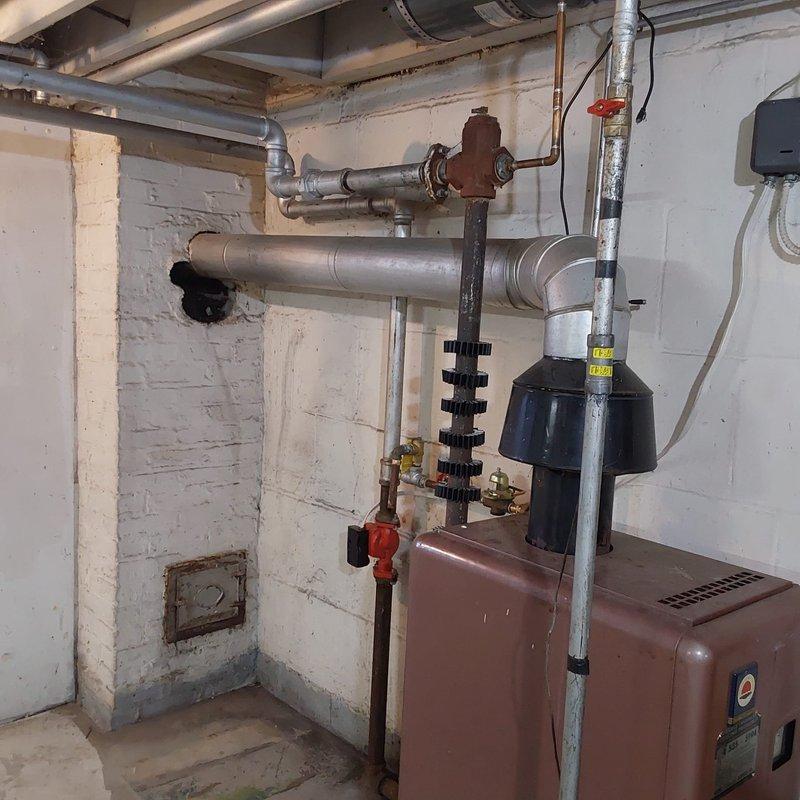 Completed full boiler replacement in basement mechanical room, removing existing heating unit and installing new brown/rust-colored boiler system with comprehensive piping infrastructure. Integrated instant hot water capability into the system, configuring extensive network of supply and return lines including copper and metallic silver pipes of various diameters with appropriate shutoff valves and controls. Installed black expansion tank with proper mounting to accommodate system pressure fluctuations, secured all piping with professional-grade fasteners and cable ties to ensure stability and code compliance. Verified all connections, performed system startup and testing to confirm proper operation of both heating and instant hot water functions.