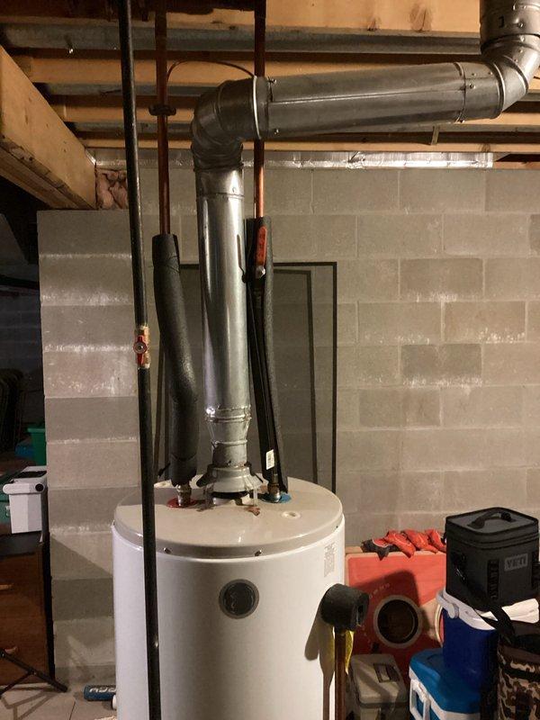 Responded to service call for water heater replacement in residential basement utility area. Upon arrival, assessed existing white cylindrical tanked water heater and surrounding plumbing connections. Completed full replacement of water heater unit, including disconnection and removal of old unit, installation of new tanked water heater, and reconnection of all supply lines, drain valves, and venting systems. Verified proper flue pipe connections to existing ductwork and ensured all metal piping connections at top of unit were secure and code-compliant. Tested water heater operation and confirmed system functionality before completing service.