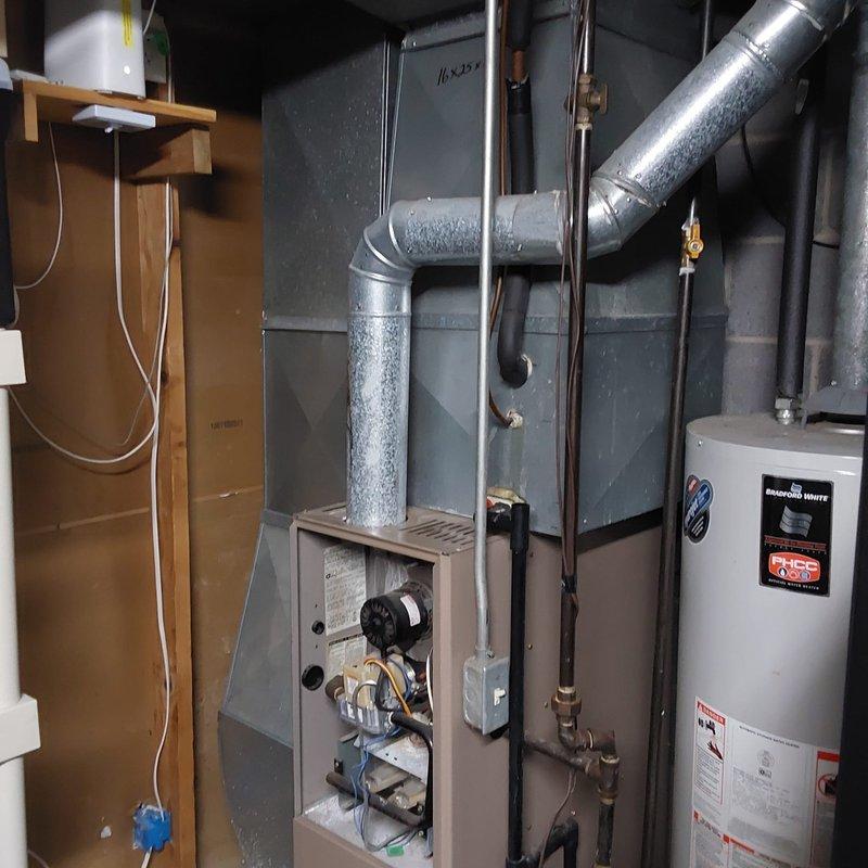 Conducted site evaluation for complete furnace and air conditioning system replacement at residential property. Assessed existing outdoor condensing unit positioned on concrete pad with electrical disconnect and conduit installation. Evaluated indoor furnace system located in basement mechanical room, including ductwork configuration with visible moisture accumulation and proximity to water heater. Documented current equipment conditions and discussed available equipment options including Lennox brand systems for replacement consideration.