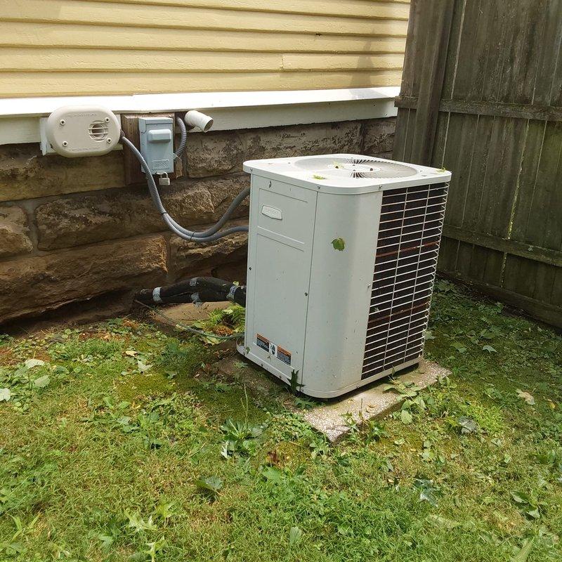 Completed full HVAC system retrofit including replacement of indoor furnace unit and outdoor air conditioning condenser. Installed new beige-cased furnace in basement utility area with proper venting using white PVC piping and insulated connections. Configured copper refrigerant lines and white ductwork for optimal airflow. Positioned new white vertical condenser unit on concrete pad against building exterior with finned coil heat exchanger. Connected unit to building electrical system using gray conduit and routed white PVC condensate drainage line through stone foundation. All components installed per manufacturer specifications and local code requirements. System tested and confirmed operational.