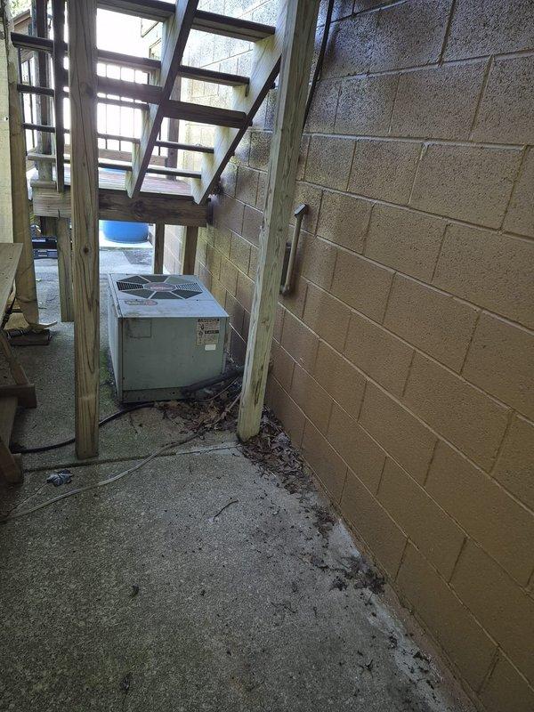 Responded to service call for air conditioning system with unknown unit age. Upon arrival, located outdoor condenser unit in covered exterior utility area showing signs of weathering and debris accumulation around base. Inspected indoor furnace and air handler system in basement utility room, noting standard equipment configuration with ductwork, refrigerant lines, and condensate management components in place. Performed diagnostic evaluation of AC system operation and documented equipment condition through photography for service records.
