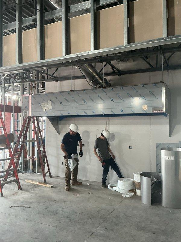 Completed commercial HVAC new construction installation including hanging range hood with roof venting, running control wiring, finishing spiral ductwork, installing economizer pop-out, and mounting power exhaust unit. All ductwork, refrigerant lines, and mechanical equipment were properly secured and positioned per specifications, with control systems wired and tested for proper operation.