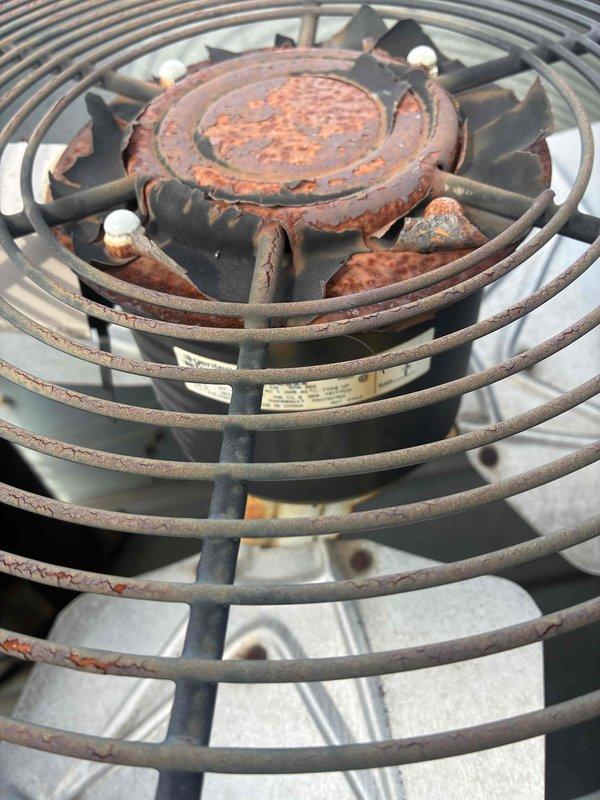Responded to emergency service call for commercial air conditioning system failure shortly after recent preventive maintenance visit. Upon arrival, conducted thorough diagnostic assessment of rooftop unit. Inspected condenser fan motor assembly and found Siemens motor (Model 45CG10AJDB1H66) operational but noted significant deterioration of outdoor unit components. Observed extensive rust and corrosion on condenser fan guard, fan blades, and central hub assembly, indicating prolonged weather exposure and potential compromised structural integrity. Evaluated electrical connections and wiring conditions at motor housing. Documented equipment condition with photographs for records and future reference. Advanced age and severe corrosion of outdoor components may be contributing factors to system reliability issues despite recent maintenance service. Recommended comprehensive evaluation of condenser unit replacement due to extensive corrosion affecting critical components.