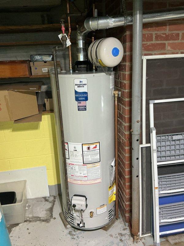 Completed installation of a 50-gallon short Bradford White residential water heater in basement utility area. Established all necessary plumbing connections including copper supply lines, discharge piping, and pressure relief valve. Connected gas supply line with shutoff valve and installed proper venting system using metallic ductwork routed through existing infrastructure. Mounted expansion tank at top of unit and verified all connections for proper operation and code compliance.