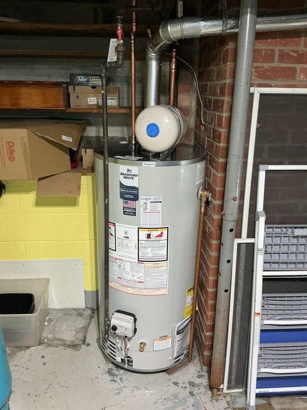 Completed installation of a 50-gallon short Bradford White residential water heater in basement utility area. Established all necessary plumbing connections including copper supply lines, discharge piping, and pressure relief valve. Connected gas supply line with shutoff valve and installed proper venting system using metallic ductwork routed through existing infrastructure. Mounted expansion tank at top of unit and verified all connections for proper operation and code compliance.