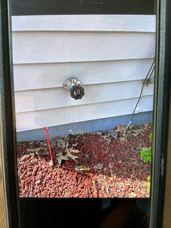 Replaced deteriorated galvanized water line with PEX tubing and installed new outdoor spigot with boiler drain valve. Access was gained through ceiling opening to remove old galvanized piping that could not be unthreaded, then ran new PEX line to exterior wall and mounted chrome-bodied hose bib with cross-handle valve on white vinyl siding.