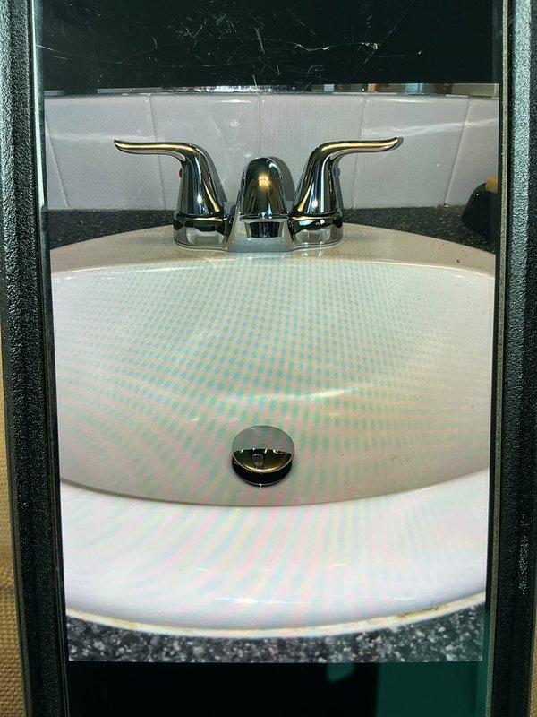 Provided estimate for installation of two-handle chrome Emerson faucet assembly on existing bathroom sink. Replacement of existing 4-20 inch flexible braided supply lines required to accommodate new fixture specifications. Documented current under-sink plumbing configuration including P-trap assembly and existing supply line connections for accurate material sizing and installation planning.