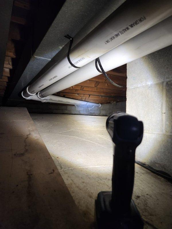 Completed furnace retrofit installation in crawl space/basement area. Installed new gray metal air handler unit with proper venting system utilizing white PVC piping secured to ceiling joists with appropriate strapping. Configured condensate drainage system with multiple PVC drain lines running from unit to designated discharge point. Connected black flexible ductwork to air handler for proper air distribution throughout structure. Verified all manufacturer specifications and safety requirements met, with proper labeling visible on equipment. Installation includes condensate pump mounted at base of unit for efficient moisture removal. All piping connections sealed and tested for leaks, with copper and gas lines properly routed along ceiling joists per code requirements.