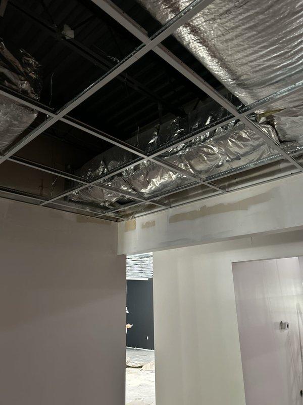 Completed ductwork insulation wrap installation in new construction project. Applied reflective insulation material to exposed metal ductwork in ceiling cavity above drop ceiling system to improve energy efficiency and prevent condensation. Verified proper coverage and secure attachment of all insulation materials throughout the installation area.