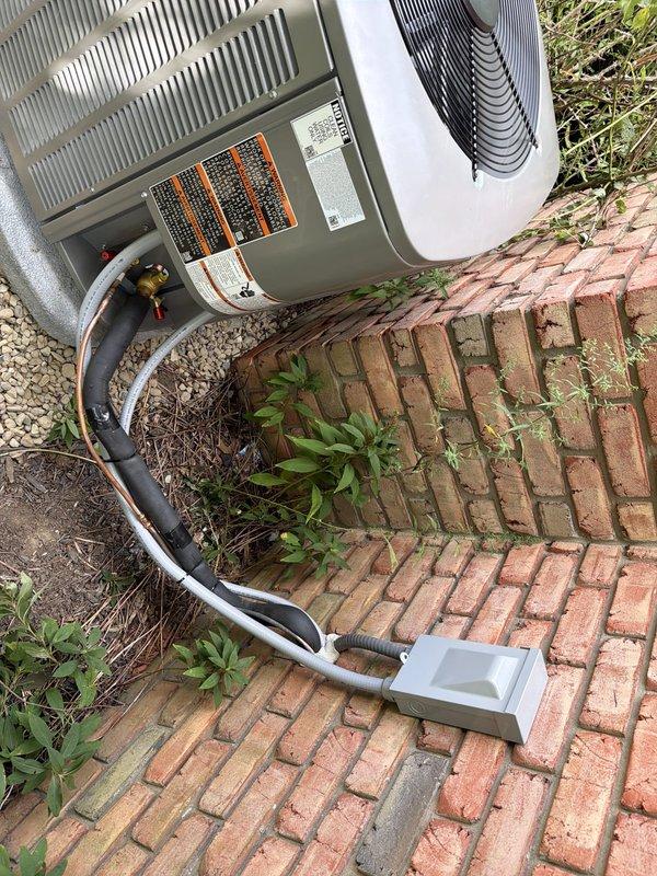 # HVAC Install - A/C & Coil

Completed full AC retrofit at residential property, replacing existing York condenser unit with new system. Removed old outdoor condensing unit from overgrown area against brick wall and relocated new equipment to improved position on brick paver pathway with proper clearances. Installed new evaporator coil inside air handler to match outdoor unit capacity and refrigerant type.

Ran new refrigerant line set with appropriate insulation from outdoor condenser to indoor coil connection point. Installed gray electrical disconnect box near outdoor unit per code requirements. Evacuated refrigerant lines to proper vacuum levels and charged system to manufacturer specifications. Verified proper refrigerant pressures on both high and low sides during system operation.

Commissioned new system with full operational testing including temperature split verification, amperage draw confirmation, and airflow assessment. Cleared vegetation and debris from installation area