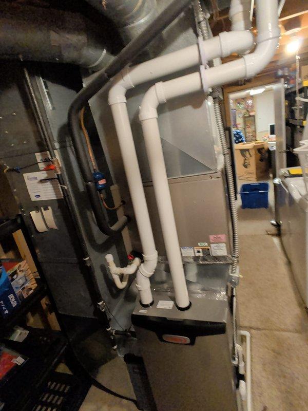 Completed furnace retrofit in residential basement utility room. Installed modern gray HVAC unit with associated white PVC condensate drain and ventilation piping, including multiple elbows and joints for proper routing. Connected black flexible ductwork and metallic flex duct to system, ensuring all connections were secure and code-compliant. Unit is operational and functioning as designed.