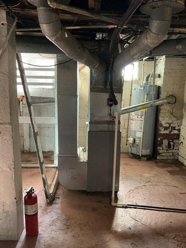 Conducted site visit for rental property where outdoor air conditioning unit was vandalized and completely gutted, with compressor and internal components stolen. Documented existing basement mechanical infrastructure including water heaters and utility routing for replacement system planning. Assessed scattered HVAC components on exterior concrete pad showing severe dismantling, with compressor unit, copper refrigerant lines, fan assembly, and metal housing panels disassembled and left exposed to elements. Photographed deteriorated equipment, rust damage on pad, and compromised refrigerant line connections. Prepared comprehensive replacement estimate for complete outdoor condensing unit and associated components required to restore cooling system to operational status.
