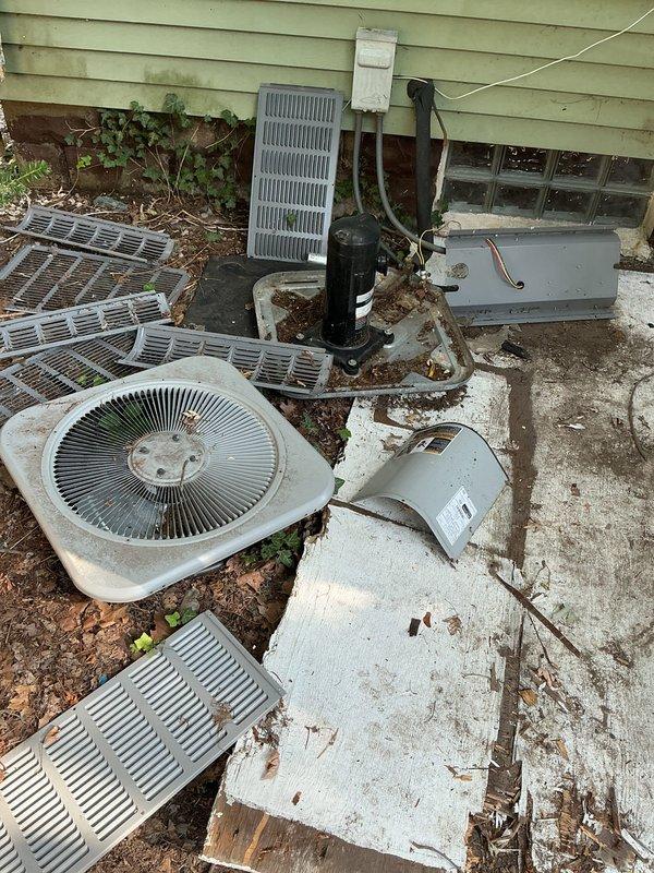 Conducted site visit for rental property where outdoor air conditioning unit was vandalized and completely gutted, with compressor and internal components stolen. Documented existing basement mechanical infrastructure including water heaters and utility routing for replacement system planning. Assessed scattered HVAC components on exterior concrete pad showing severe dismantling, with compressor unit, copper refrigerant lines, fan assembly, and metal housing panels disassembled and left exposed to elements. Photographed deteriorated equipment, rust damage on pad, and compromised refrigerant line connections. Prepared comprehensive replacement estimate for complete outdoor condensing unit and associated components required to restore cooling system to operational status.