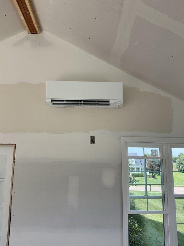 Completed rough-in installation of Mitsubishi ductless mini-split heat pump system in new construction residential property. Mounted indoor wall unit on interior wall below vaulted ceiling with proper clearances, installed exterior condenser unit on pad with appropriate spacing from existing Lennox central air system, and ran refrigerant line set and electrical connections between indoor and outdoor components. System is ready for final startup and commissioning upon completion of finish work.