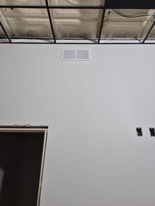 Completed installation and finishing of exhaust fan system with flexible metallic ductwork routing through exposed ceiling cavity. Installed ceiling-mounted exhaust grille with integrated fan component and wall-mounted return air vent, ensuring proper ventilation for the new construction space.