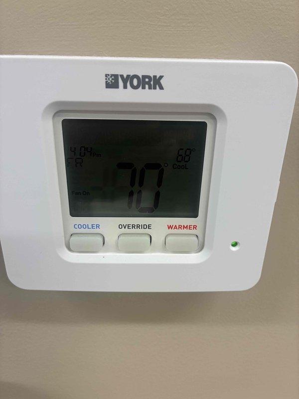 Responded to service call for commercial HVAC system with multiple zone temperature discrepancies. Found significant condensation and water leakage from ductwork in ceiling space above one zone. Inspected York thermostat showing 70°F setpoint with cooling mode active. Documented excessive condensation on main supply duct with water droplets covering entire surface, indicating inadequate insulation and likely cause of ceiling leak. System requires duct insulation repair or replacement and further evaluation of refrigerant charge and airflow balance across all zones to address uneven cooling performance between areas.