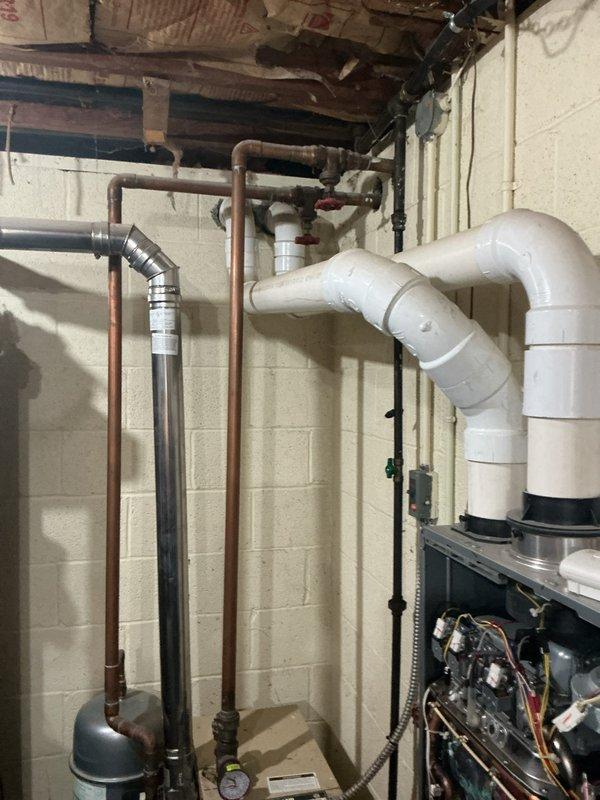 Conducted on-site assessment of existing water heating system in basement utility area to provide estimate for tankless water heater installation. Evaluated current plumbing configuration including copper supply lines, existing tank-style water heater, gas connections, and venting system. Photographed existing equipment layout, wall-mounted HVAC components, PVC drainage piping, and available installation space to determine optimal placement and required modifications for tankless unit conversion.