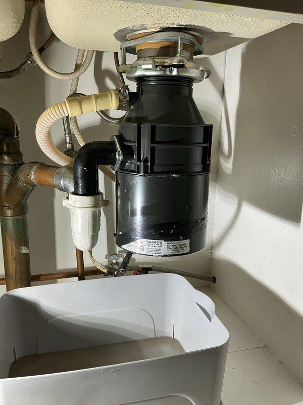 Responded to a water leak located under the kitchen sink. Upon inspection, identified the garbage disposal unit as the source of the leak. The existing disposal showed signs of failure at connection points and required replacement. Documented the faulty unit and surrounding plumbing configuration, including the dishwasher drain connection via corrugated hose, PVC discharge piping, and water supply lines. Provided photographic documentation of the defective disposal and cabinet interior for service records.