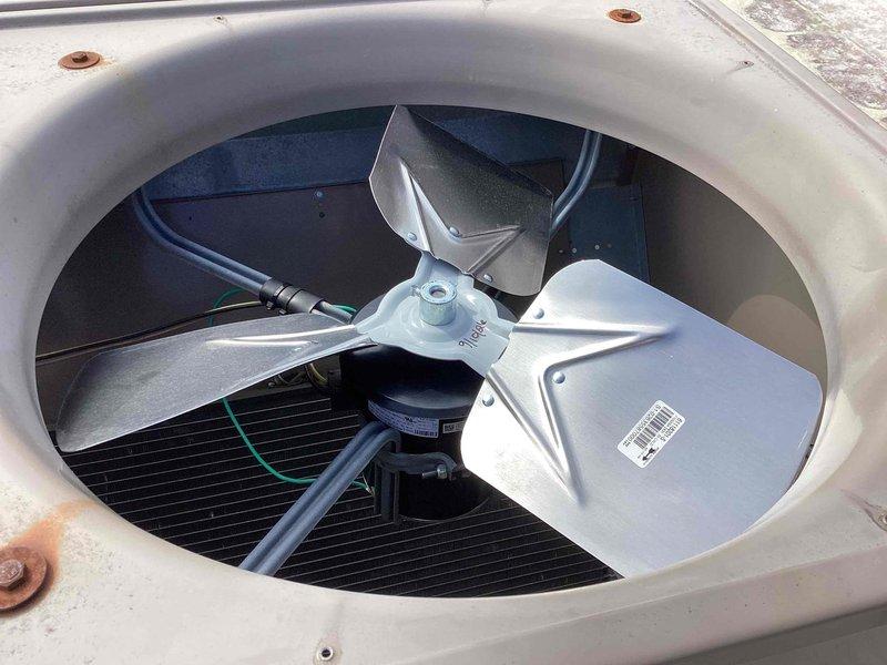 Replaced failed condenser fan motor, fan blade, and run capacitor on commercial air conditioning unit. Verified proper operation with temperature readings and confirmed new fan assembly spinning freely with adequate airflow through protective grille.