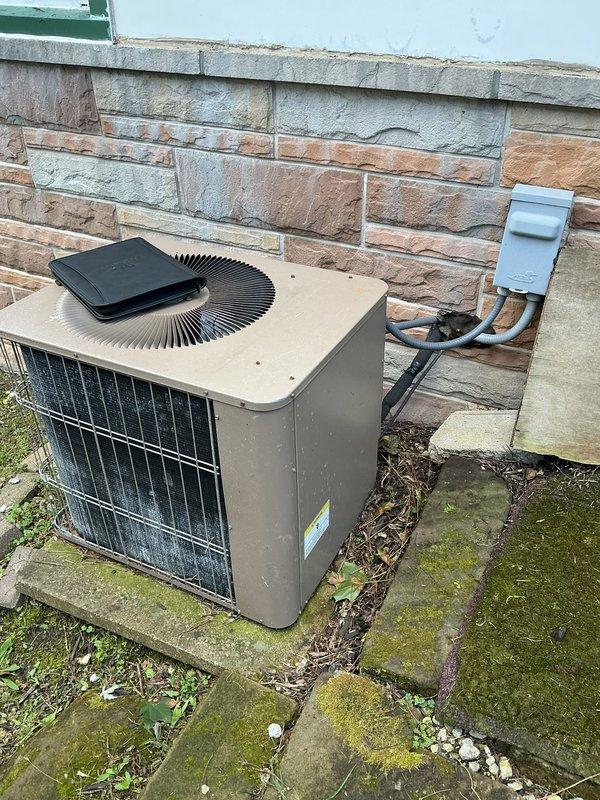 Completed furnace retrofit installation in residential basement utility room. Replaced existing heating unit with new furnace system, including proper venting configuration using PVC exhaust and intake piping routed through wooden platform support structure. Verified all connections to existing ductwork and ensured proper clearances from water heater and surrounding utilities. Exterior condenser unit remains in service on concrete pad adjacent to building exterior with stone veneer siding, connected via refrigerant lines for cooling operation. System tested and operational upon completion.