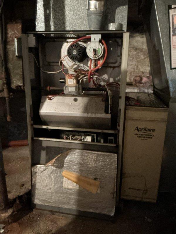 Completed furnace retrofit installation of Aprilaire HVAC system in basement utility area. Unit was properly positioned with access panels opened for final inspection of blower motor assembly, electrical connections, and control mechanisms. Verified all internal components including red motor wiring, mounted controls, and metallic vent piping extending from unit top are secured and functioning per manufacturer specifications.