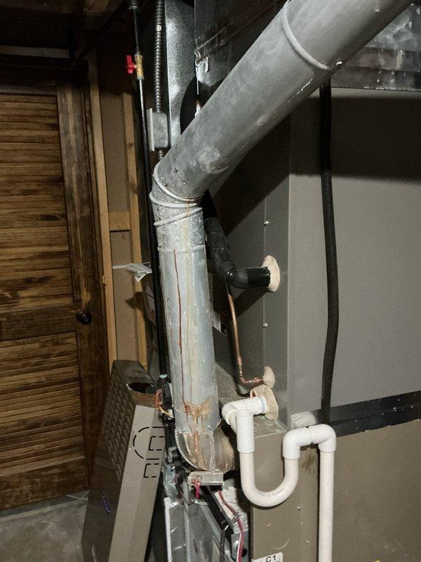 Completed furnace retrofit installation in basement utility area. New gray metal cabinet furnace unit installed against wall with proper PVC condensate drainage system, white insulated supply ductwork, and black flexible exhaust piping secured with metal clamps. All components properly connected and positioned for optimal operation in accordance with manufacturer specifications.