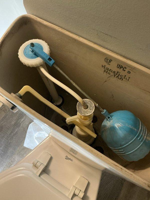 Responded to a water leak originating from a second-floor toilet that was causing damage to the ceiling below. Upon inspection, identified the fill valve assembly as the source of the leak, with visible mineral deposits and wear on the internal tank components. Documented the wall-mounted tank system, water supply connections, and shutoff valve configuration, noting the Mansfield toilet tank model and existing plumbing setup for potential repair or replacement of the faulty fill valve mechanism.