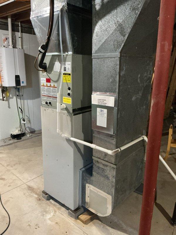 Completed furnace retrofit installation in residential basement utility room. Replaced existing heating system with new vertical furnace unit and integrated air handler assembly. Installation included proper mounting on concrete pad, connection of supply and return ductwork to existing plenum system, and integration with horizontal PVC condensate drainage piping. Verified all electrical connections to panel, ensured proper clearances per manufacturer specifications, and confirmed system operational functionality. Unit positioned alongside existing ductwork infrastructure with flexible ducting routed to ceiling distribution points.