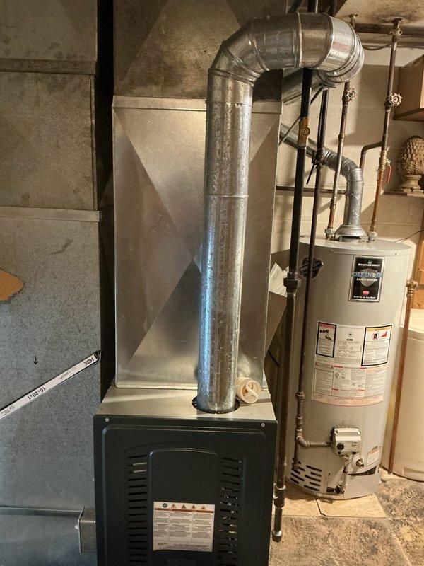 Completed AC retrofit at residential property involving assessment and documentation of existing HVAC system configuration. Inspected and photographed basement heating unit with connected ductwork and outdoor condensing unit showing age-related wear. Documented current equipment placement, electrical connections including disconnect box, and system layout to prepare comprehensive replacement estimate for aging air conditioning system.