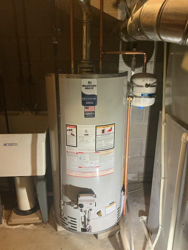 Completed installation of a 50-gallon Bradford White gas water heater in basement utility area. Installed unit on concrete floor with proper connections including copper supply lines, gas line, and venting through existing ductwork. Configured all plumbing connections with appropriate fittings and ensured proper drainage lines were in place. Verified all safety labels and warning tags were visible and unit was secured according to manufacturer specifications and local code requirements.